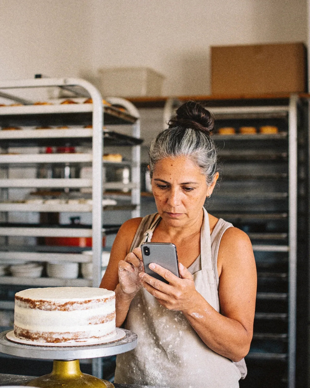 Pastelera mirando el celular junto a una torta