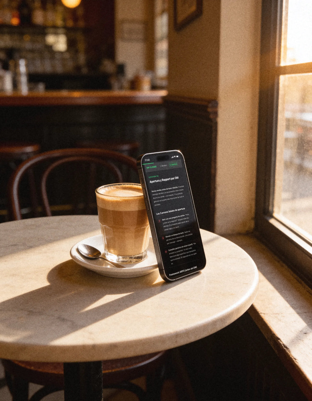 Celular apoyado en una taza de café, con la lección 2 del curso abierta en la pantalla
